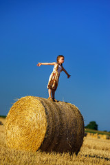 Naklejka na ściany i meble Funny cute little girl posing on the haystack in summer field