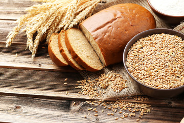 Ears of wheat and bowl of wheat grains on brown wooden backgroun