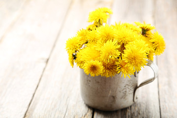 Yellow dandelion in cup on grey wooden background