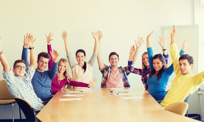 group of smiling students raising hands in office