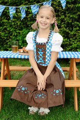 Kind im Biergarten trägt Dirndl als bayerische Tracht zum Oktoberfest