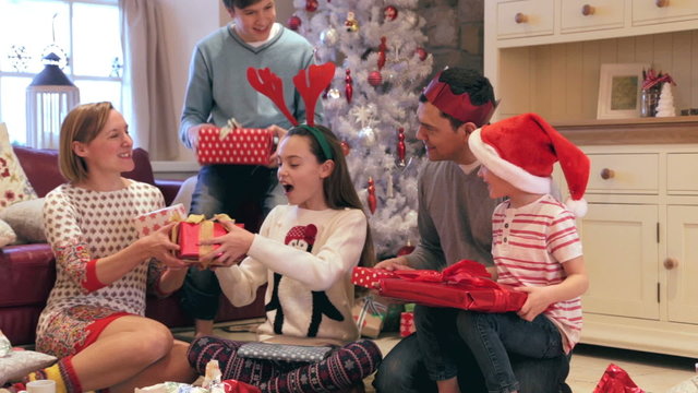 Family at christmas time trying to guess what their presents are before they open them. They are sitting together on the floor near the christmas tree in their home.