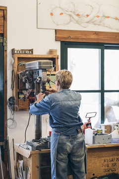 Senior woman artist fixing on drilling machine in workshop