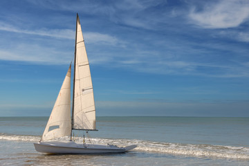little white sailboat grounded on a beach on blue cloudy background