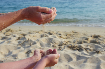 Mother and the son pour sea sand from hand to hand on a beach.Hands of the man and the child with sand