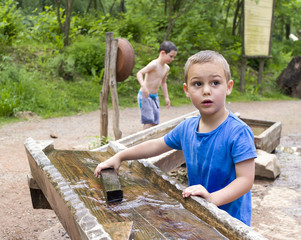 Children playing with water in wooden fountain in park or natural playground