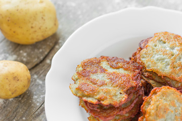potato fritters/ hash browns with a golden crust in a white ceramic plate and a crude potato on the old gray burst board