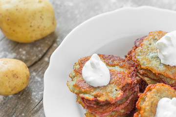 hash browns/ hash browns with a golden crust with sour cream in a white ceramic plate and a crude potato on the old gray burst board