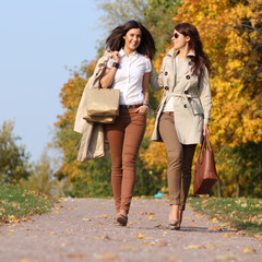 Two attractive women with autumn maple leaves in park at fall ou