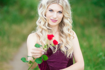 Beautiful young blonde woman with curly hair holding a basket full of red roses. Soft focus