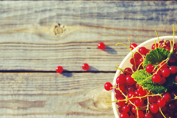 Berries of red currant in a white bowl on a textural wooden surface.