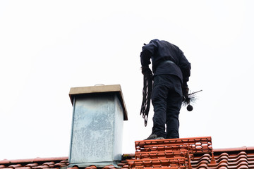 Kaminkehrer oder Schornsteinfeger kehrt Schornstein auf Haus