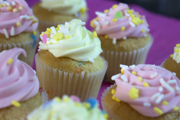 This is a photograph of Vanilla cupcakes topped with Pink and Yellow buttercream,and colorful sprinkles