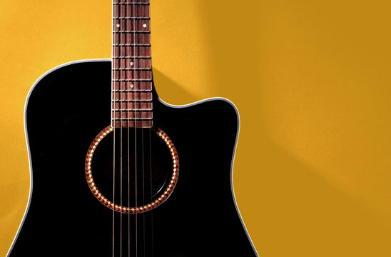 Black acoustic guitar on yellow wall, with shadow