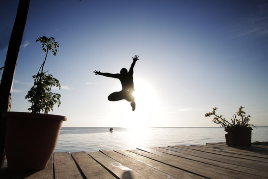 Silhouette View Of A Man Jump From A Dock To The Open Sea Water In Sunset