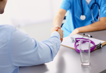 Attractive female doctor shaking a patient's hands in her office