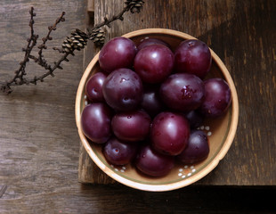 Bowl with plums, top view, on a wooden background