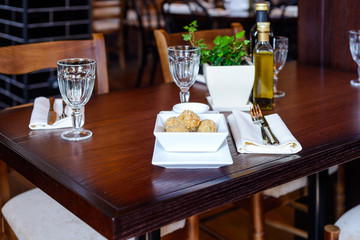 Vegetarian dish of balls of fried potatoes at the restaurant/Dish of potato balls, cutlery, napkins and wine glasses on a wooden table in a restaurant