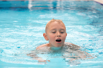 Fototapeta na wymiar A cute blonde boy swimming in a swimming pool