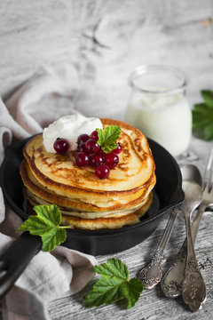pancakes with honey, sour cream and red currants in a vintage scourage on a light wooden background