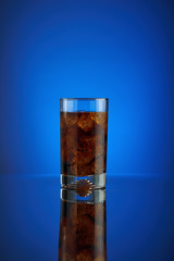 Cola soft drink on a blue background. Refreshing  liquid soda drink coca pouring into a glass with ice. Pour high speed beverage for promoting restaurant and bar. Closeup isolated design liquor.
