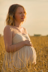 Portrait of a pregnant woman in a field of ripening wheat as a symbol of fertility