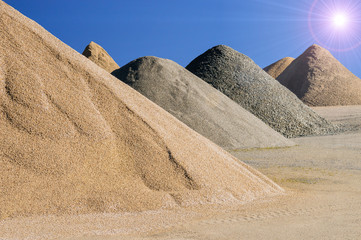 Materiallager Bruchstein und Splitt als kegelförmige Haufen vor blauem Himmel mit Sonne