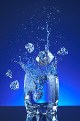 Ice and Water poured into a glass, splash, blue background, refreshing, freshness and health. blue liquid, ice, drops, motion, wave, splash, transparent blue water,
