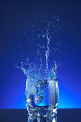 Water poured into a glass, splash, blue background, refreshing, freshness and health. Blue liquid, ice, drops, motion, wave, splash, transparent blue water,
