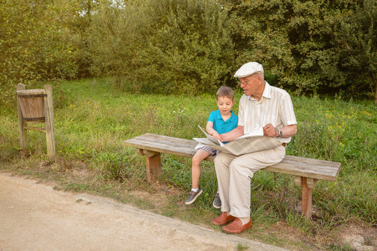 Senior man and child reading a newspaper outdoors
