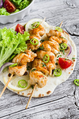 chicken kebabs and fresh vegetable salad on a homemade tortilla on a light wooden background