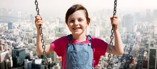 happy little girl swinging on swing over city