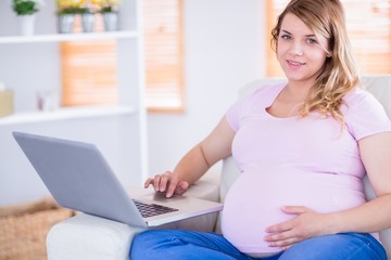 Pregnant woman looking at camera and using laptop
