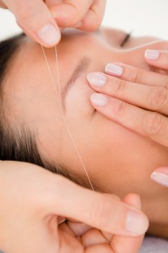 Hands threading beautiful womans eyebrow