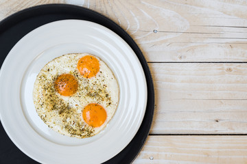Plate with fried eggs on black tray, wooden table