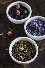 Assortment of dried tea in white bowls on vintage dark surface