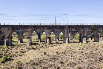 Railway train bridges concrete arched structures across dry river landscape in vintage travel