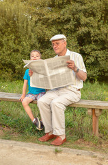 Senior man and bored child reading newspaper outdoors