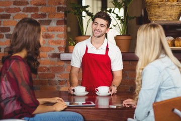 Smiling waiter serving coffees to customers