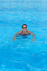 Mid adult woman is swimming in bright blue water of pool.