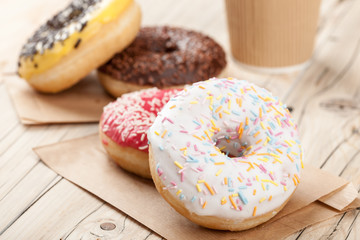 Colorful donuts and paper cup on wooden table