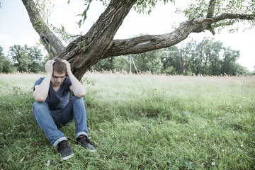Sad guy sitting under a tree