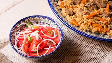 Pilaf and achichuk salad in handmade plate on wooden background