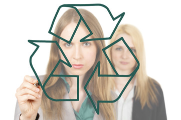 One woman holding a marker drawing a recycling symbol. A second woman looks on from behind.