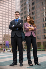 Fototapeta premium Portrait of businessman and businesswoman standing tall with arms crossed folded in front of urban setting