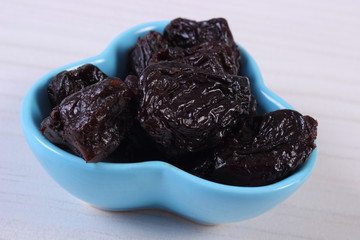 Dried plums in blue bowl on wooden table, healthy food