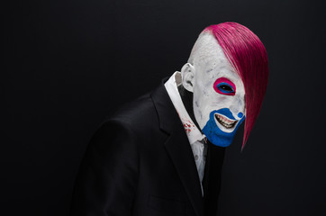 Clown and Halloween theme: Scary clown with pink hair in a black jacket on a dark background in the studio