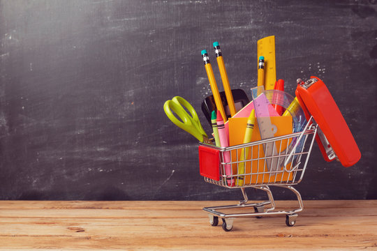 Shopping cart with school supplies over chalkboard background. Back to school sale concept