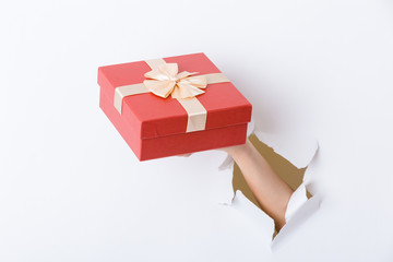 Hand holding giftbox through the hole in paper