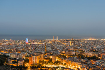 Bird's eye view of illuminated Barcelona. The panorama shows Sagrada Familia, Torre Agbar, and Port Olimpic down to the harbor.